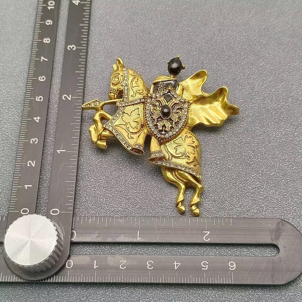 Jousting knight on horse brooch with carved golden metal accents and rhinestone detailing