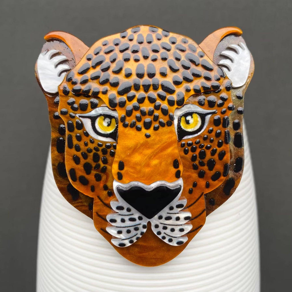 Leopard head design brooch on a white cylindrical object with a dark background