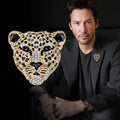 Man wearing a black suit with a gold and black jeweled leopard head brooch on a dark background