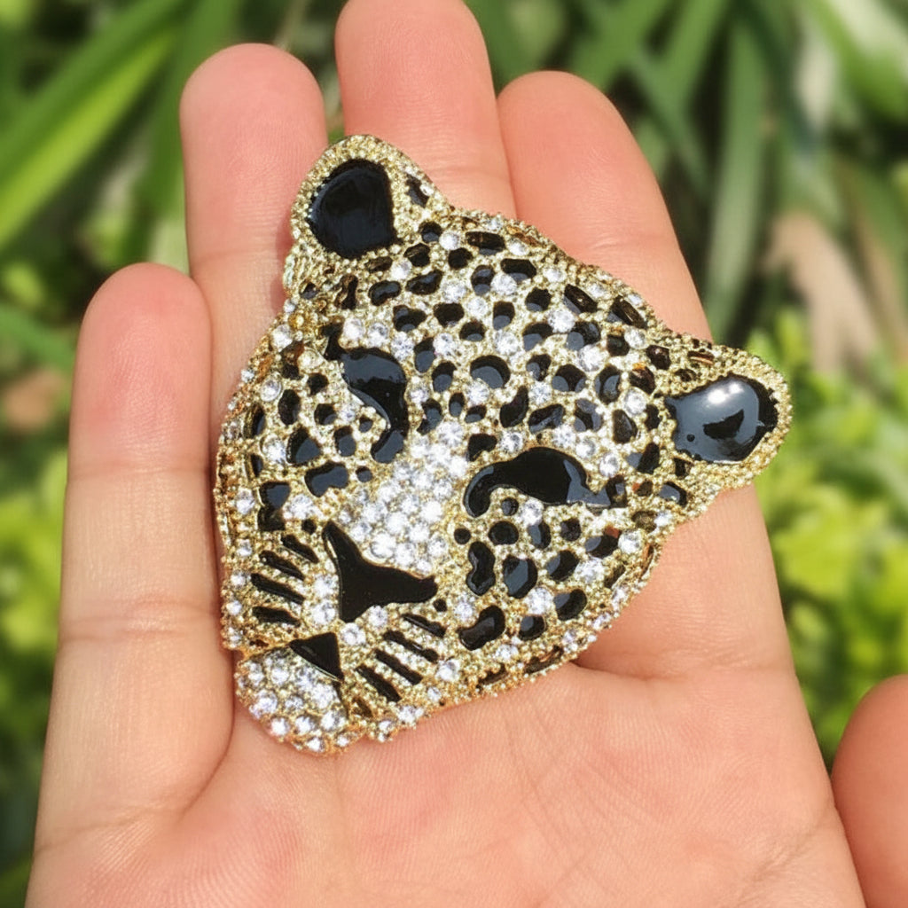 Leopard head rhinestone brooch being held in a hand against a outdoor green background