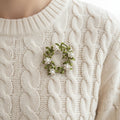 Floral brooch with green leaves and white flowers pinned on a white sweater