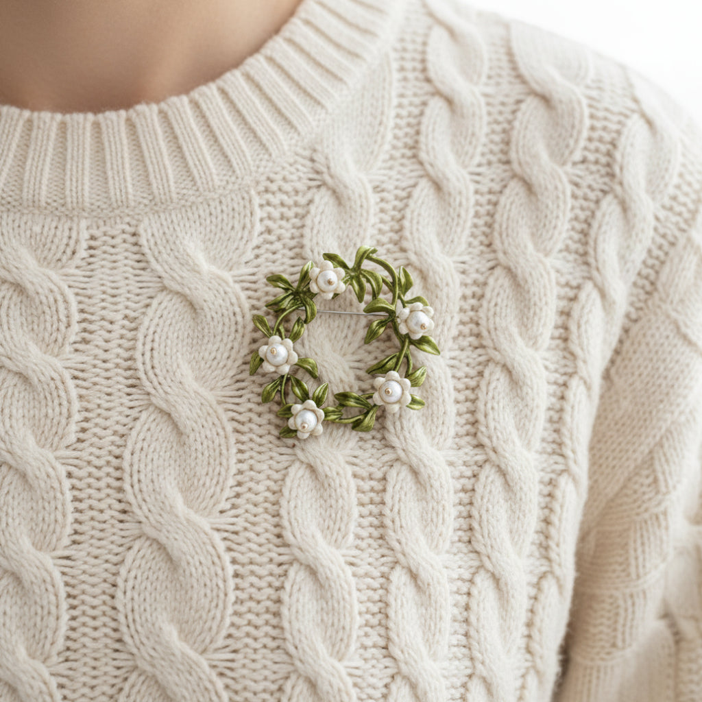 Floral brooch with green leaves and white flowers pinned on a white sweater