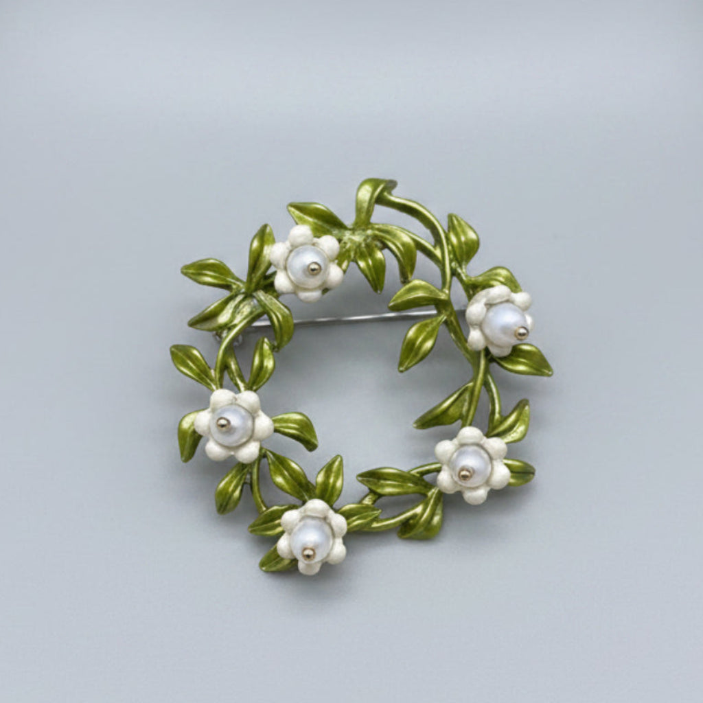 Floral brooch with green leaves and white flowers on a gray background