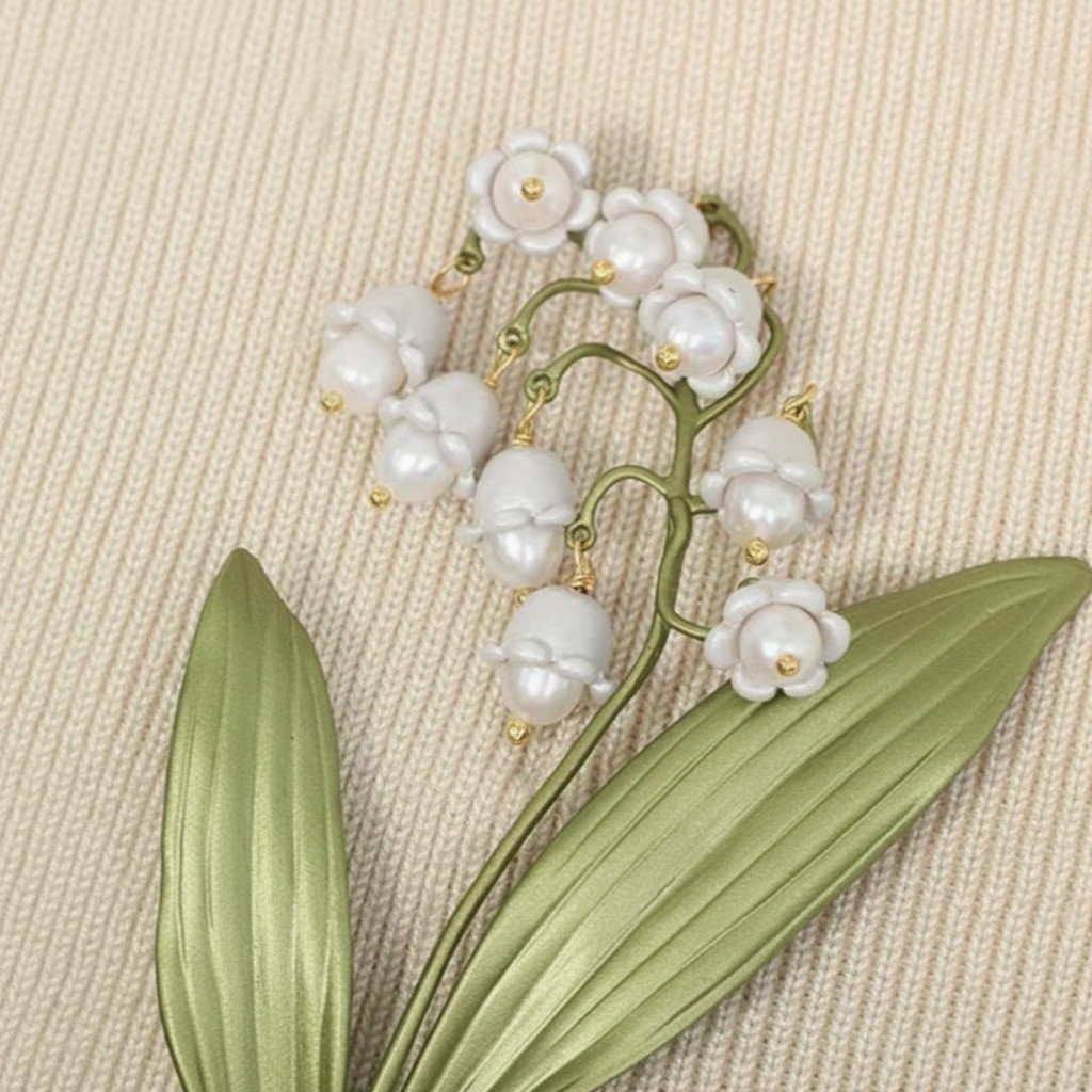 Lily of the valley plant brooch close up view against a textured cream color background