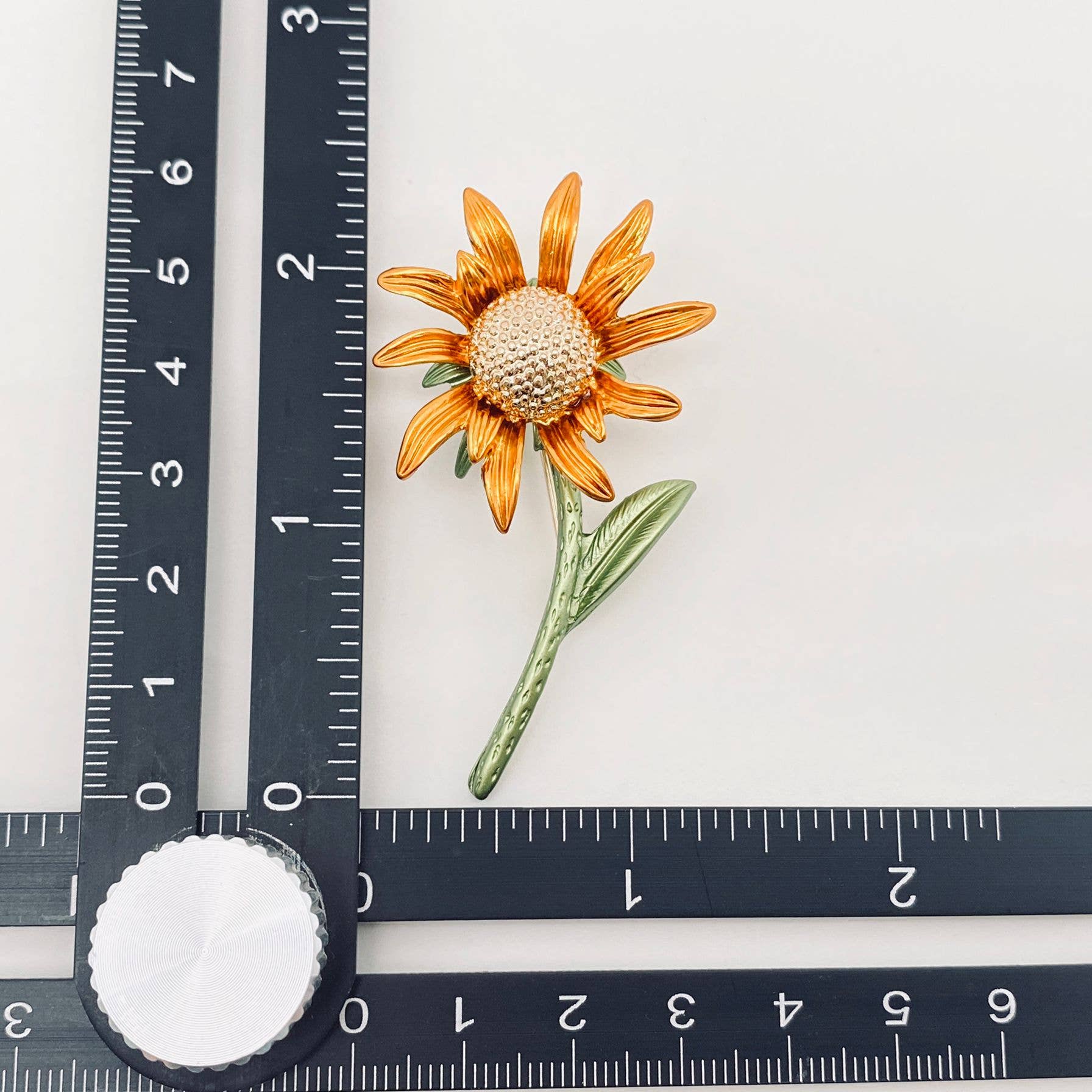 Sunflower-shaped brooch next to a ruler on a white background