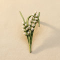 Green enamel rice plant brooch with pearl accents on a beige background