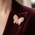 Butterfly-shaped brooch with pink center and gold and gemstone accents pinned on a burgundy suite 