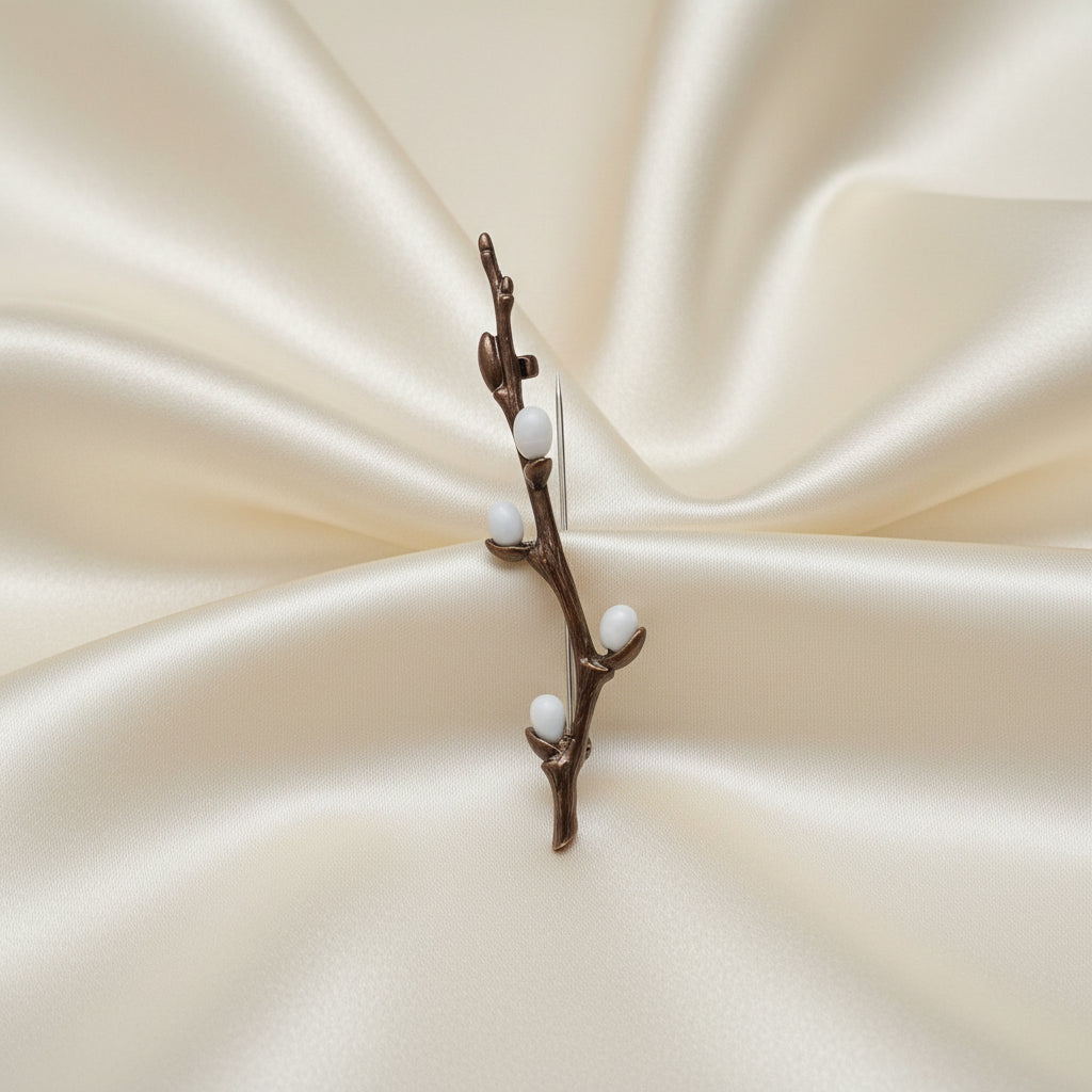 Bronze brooch with branches and small white berries on a ivory silk background