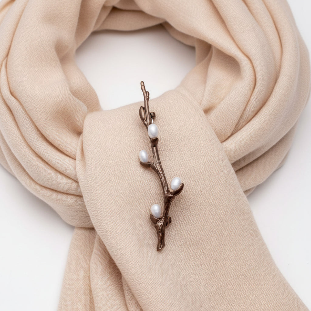 Bronze brooch with branches and small white berries pinned on a beige scarf