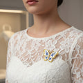 Butterfly-shaped brooch with blue and gold design on a white lace dress