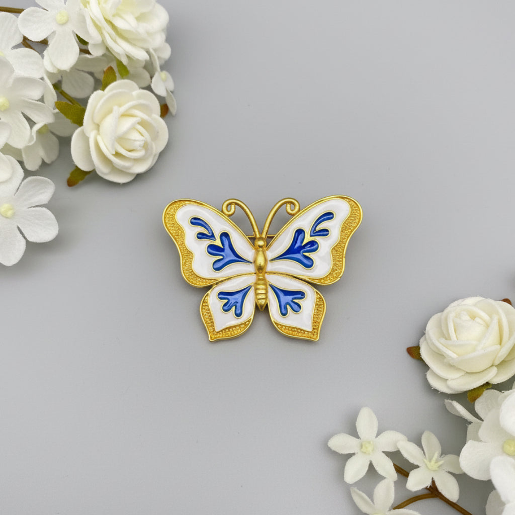 Butterfly-shaped brooch with blue and gold design on a white background