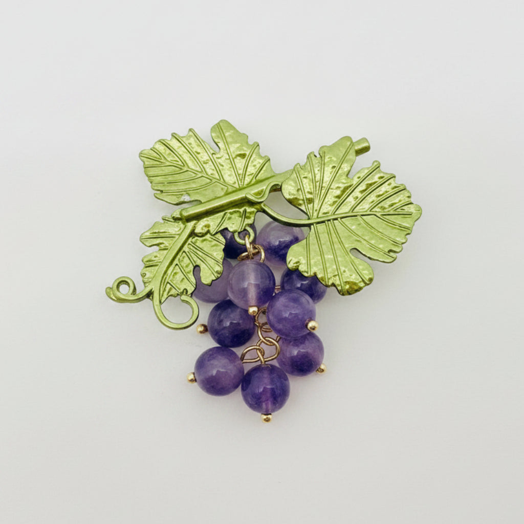 Brooch with green leaf design and purple glass stones on a gray background
