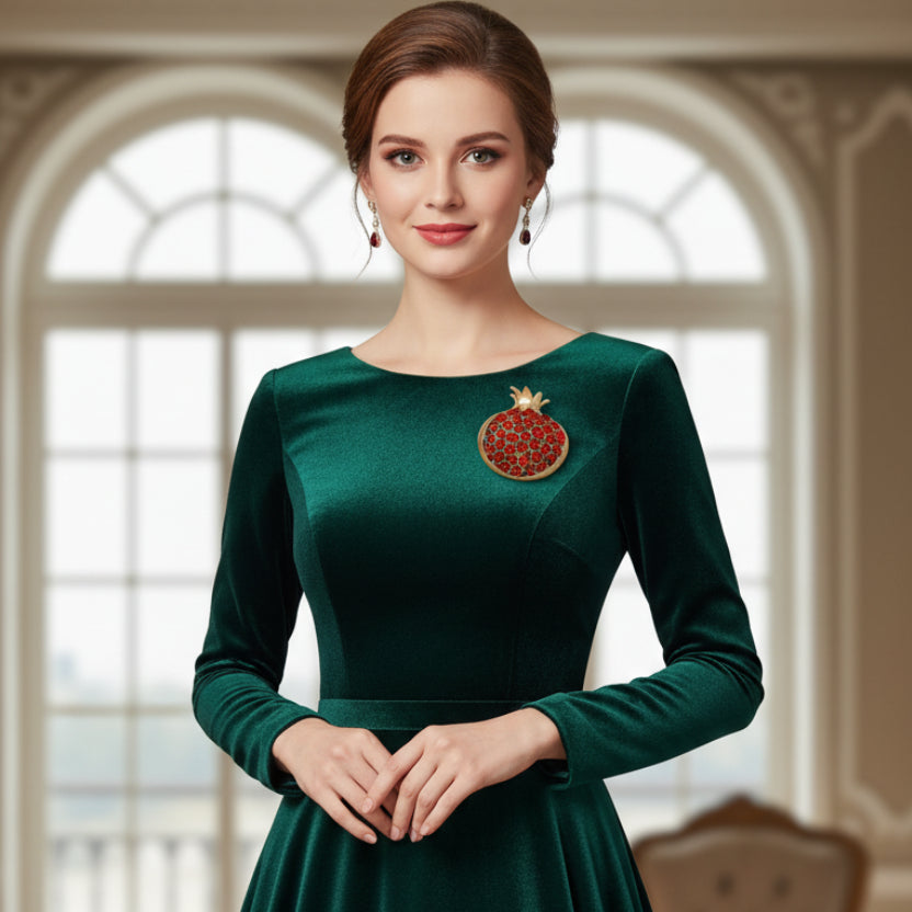 A gold-toned brooch shaped like a pomegranate, with a round cluster of red gemstones, pinned on woman's green dress