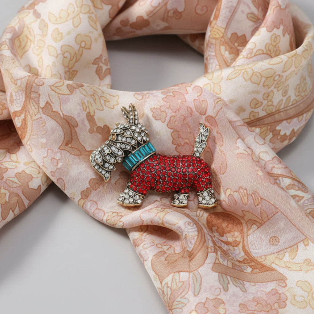 A decorative dog-shaped brooch embellished with clear rhinestones and a turquoise collar, placed on a light pink patterned scarf