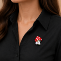 Mushroom-shaped brooch with red cap and white spots pinned on a black shirt