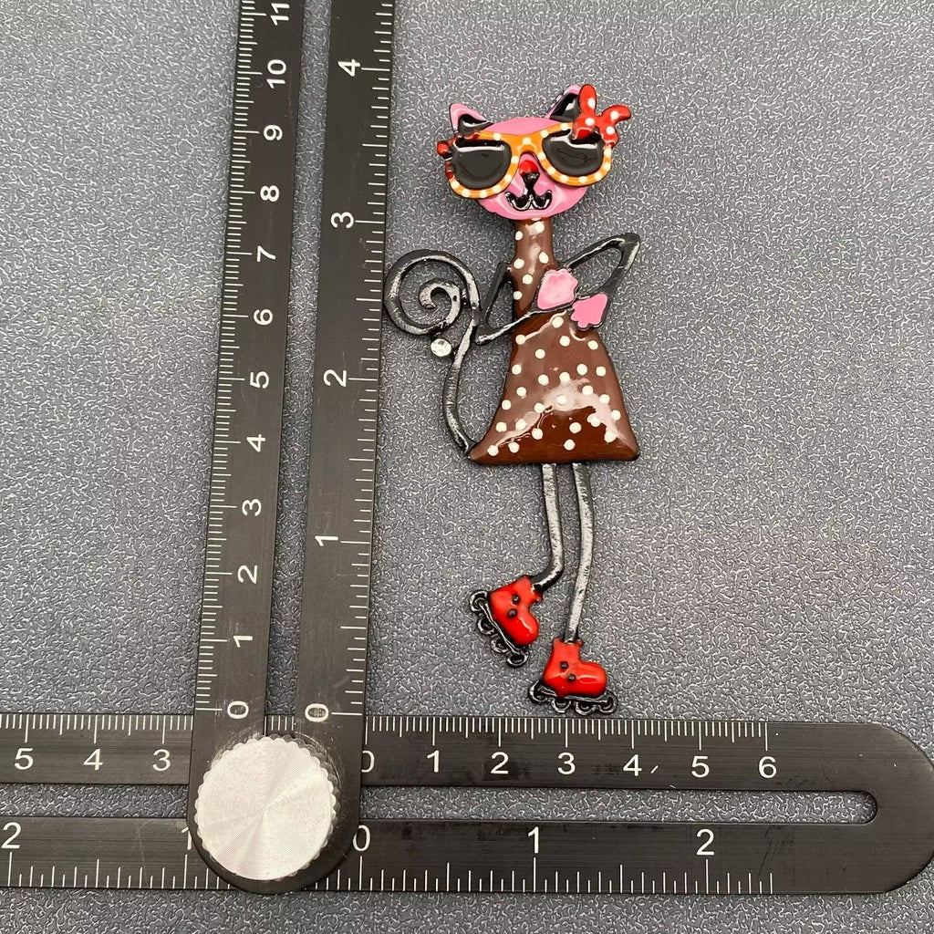 Decorative brooch of a polka dot cat with sunglasses and roller skates, measured against a ruler on a gray background