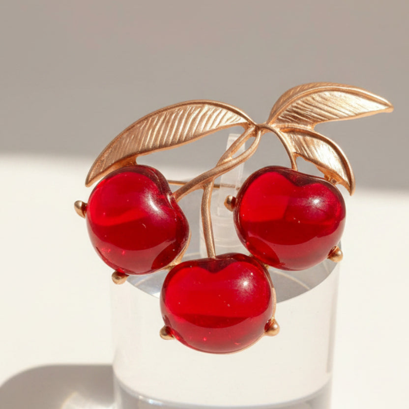 Brooch with red cherries and gold leaves on a light gray background