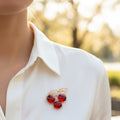 Brooch with red cherries and gold leaves pinned on a woman's ivory shirt