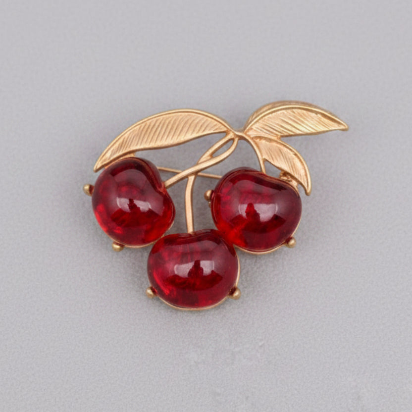 Brooch with red cherries and gold leaves on a gray background