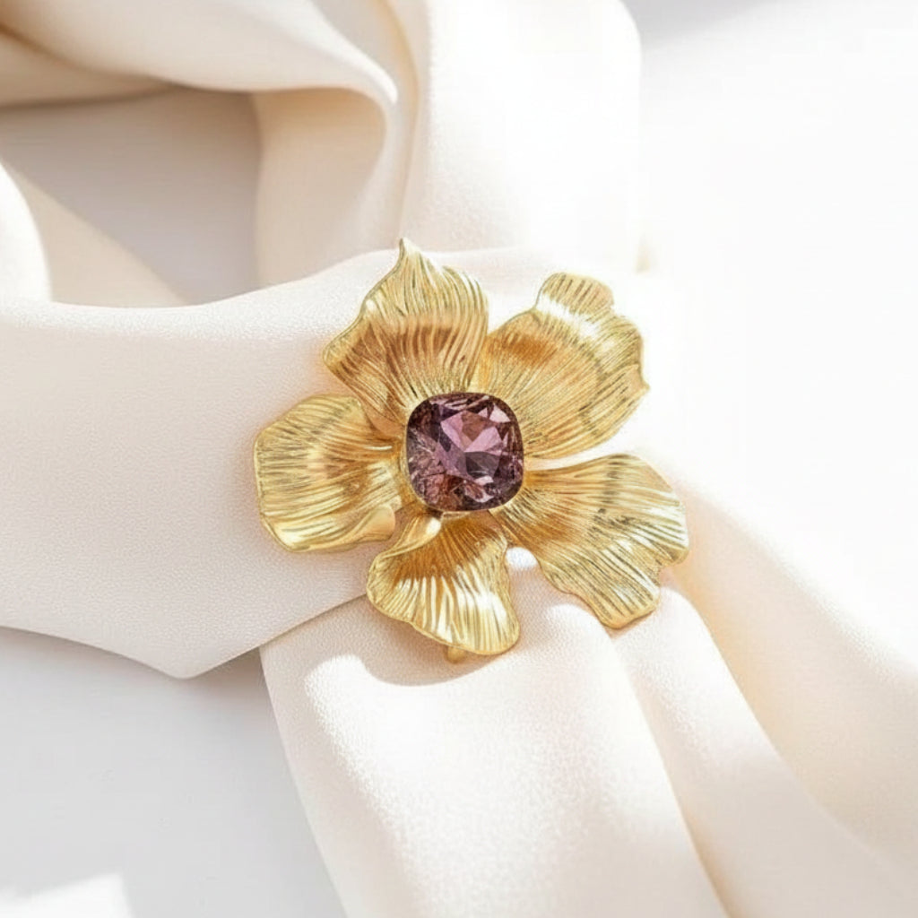 Gold flower-shaped brooch with a pink gemstone on a white background