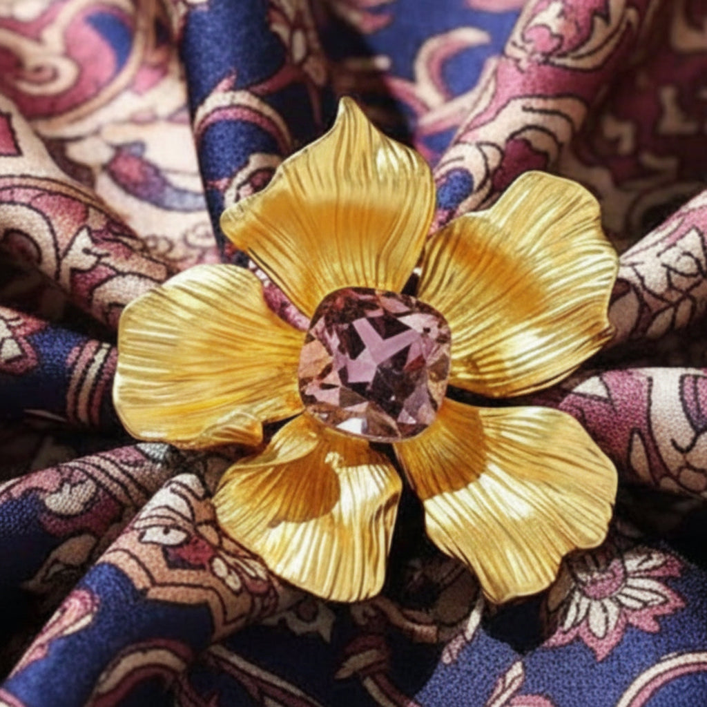 Gold flower-shaped brooch with a pink gemstone on a paisley scarf