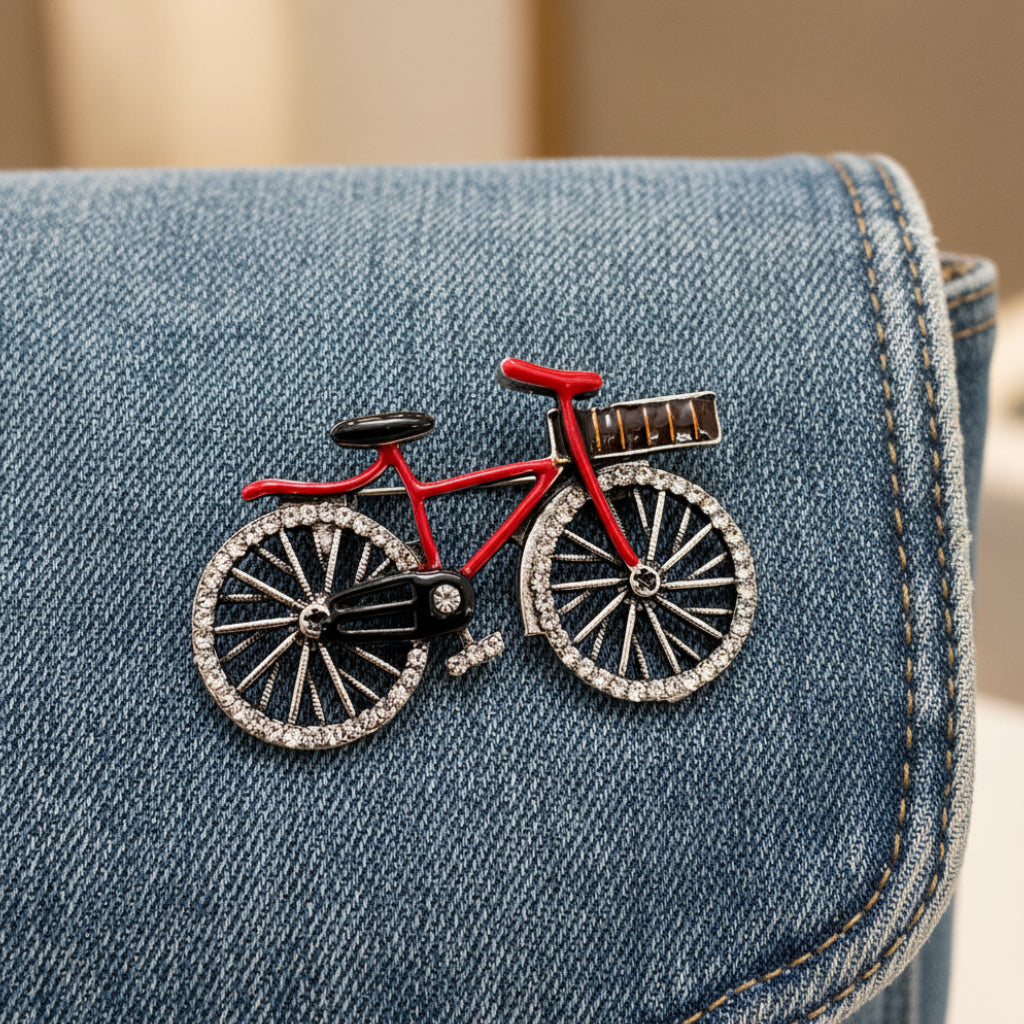 Bicycle-shaped brooch with red frame and black wheels pinned on a denim bag