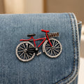 Bicycle-shaped brooch with red frame and black wheels pinned on a denim bag