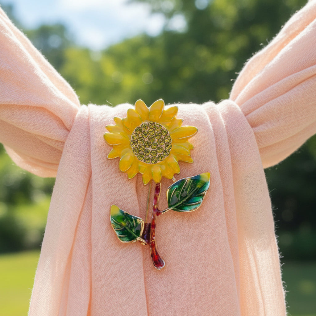 Sunflower-shaped brooch with yellow petals and green leaves, pinned on a white scarf