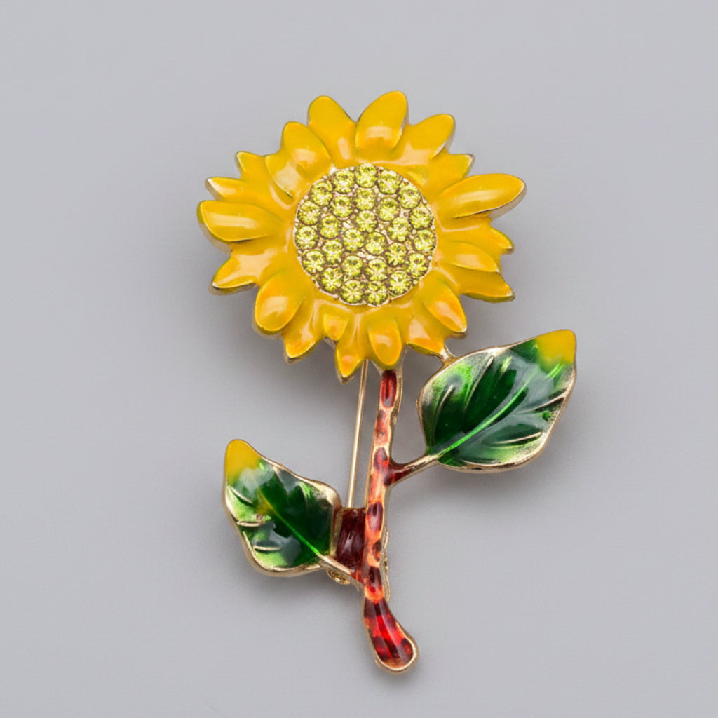 Sunflower-shaped brooch with yellow petals and green leaves on a gray background