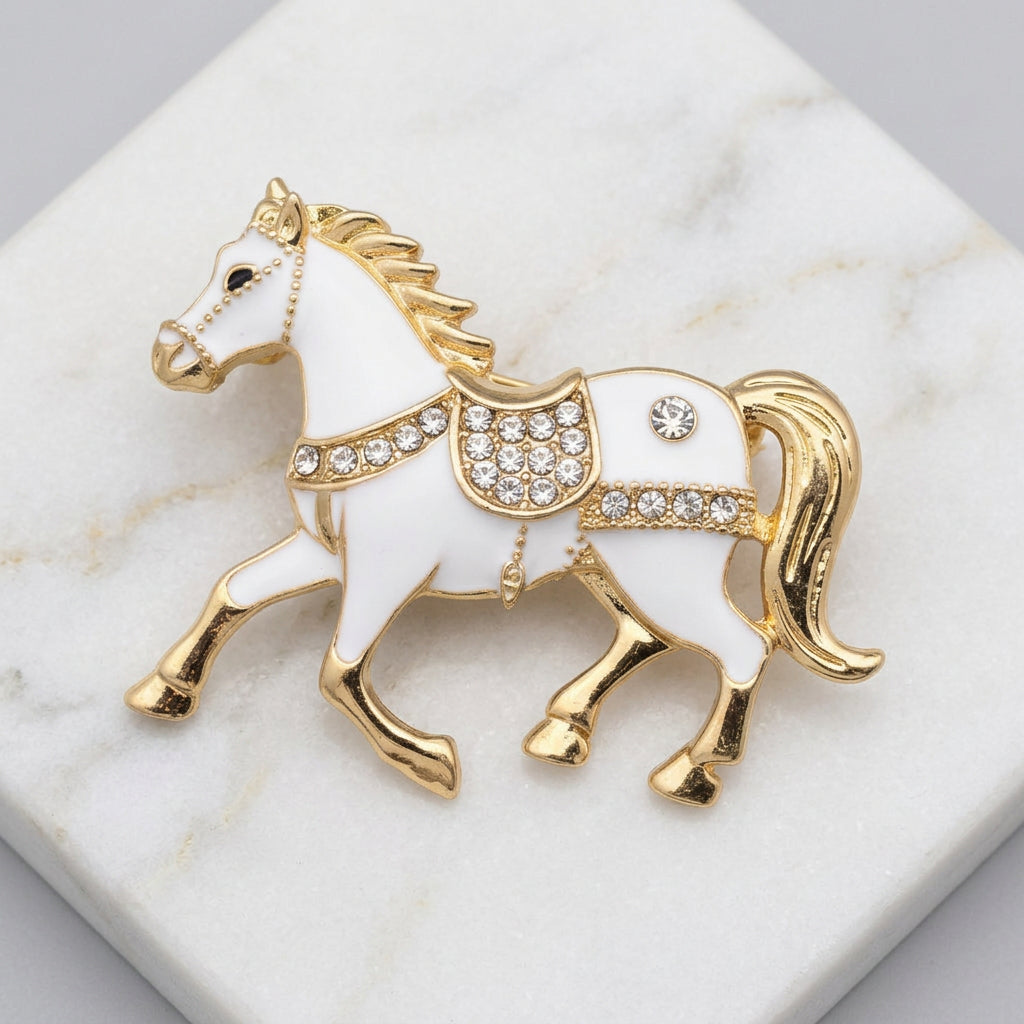 White and gold horse brooch with rhinestone accents, on a white marble background.