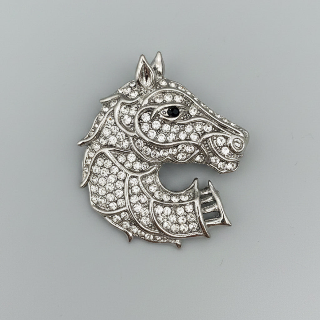 Silver horse head brooch with gemstones on a gray background