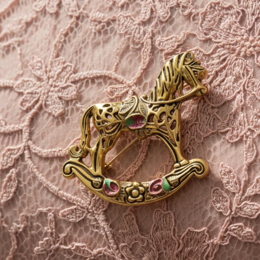 Gold rocking horse brooch with floral details on a pastel pink background