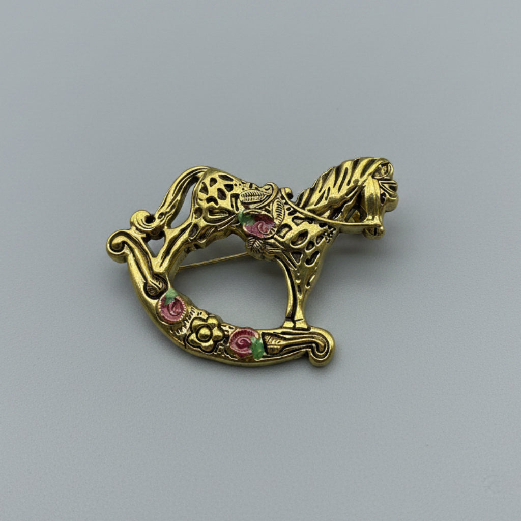Gold rocking horse brooch with floral details on a gray background