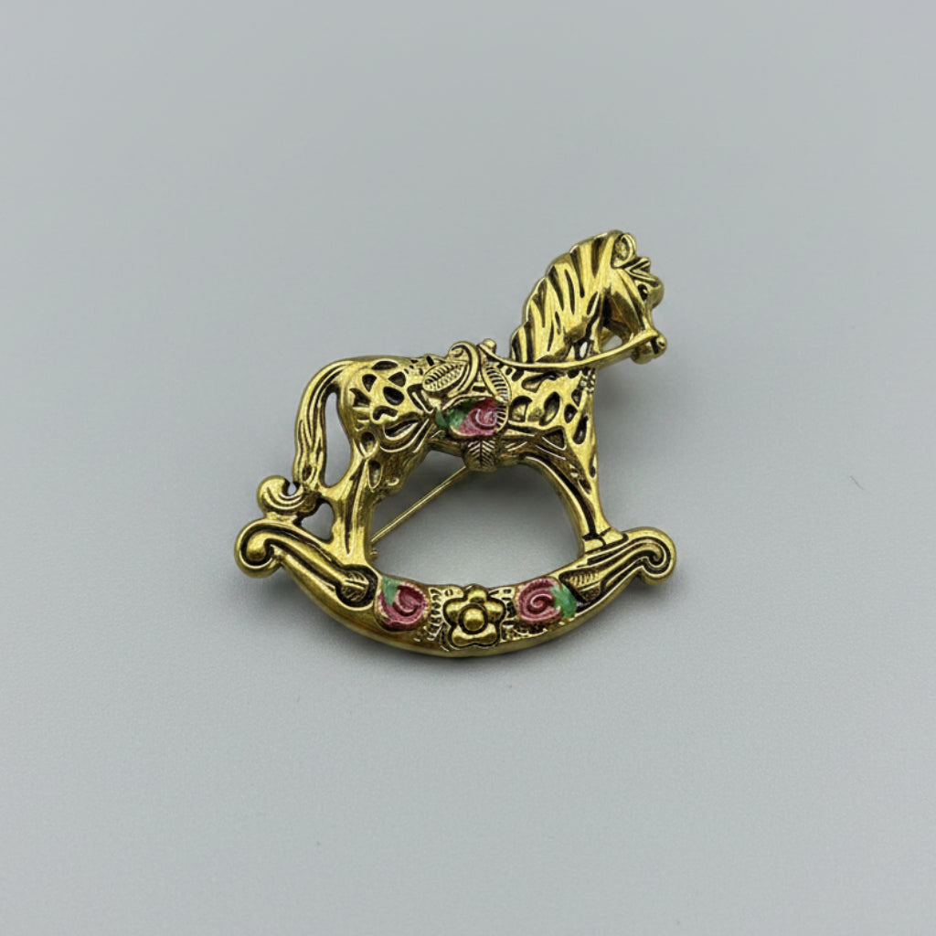 Gold rocking horse brooch with floral details on a gray background