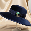 Cat-shaped brooch with green gemstone and crown pinned on a blue fancy hat