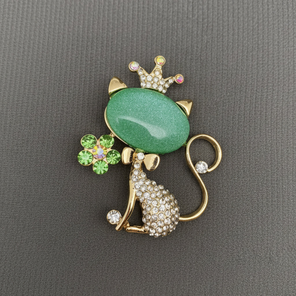 Cat-shaped brooch with green gemstone and crown on a gray background