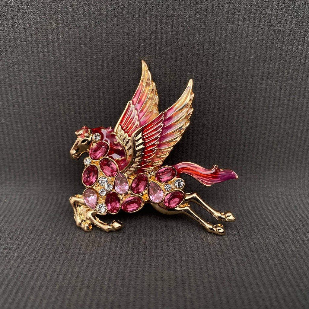 Gold pegasus brooch with ruby gemstones held in a hand against a gray background