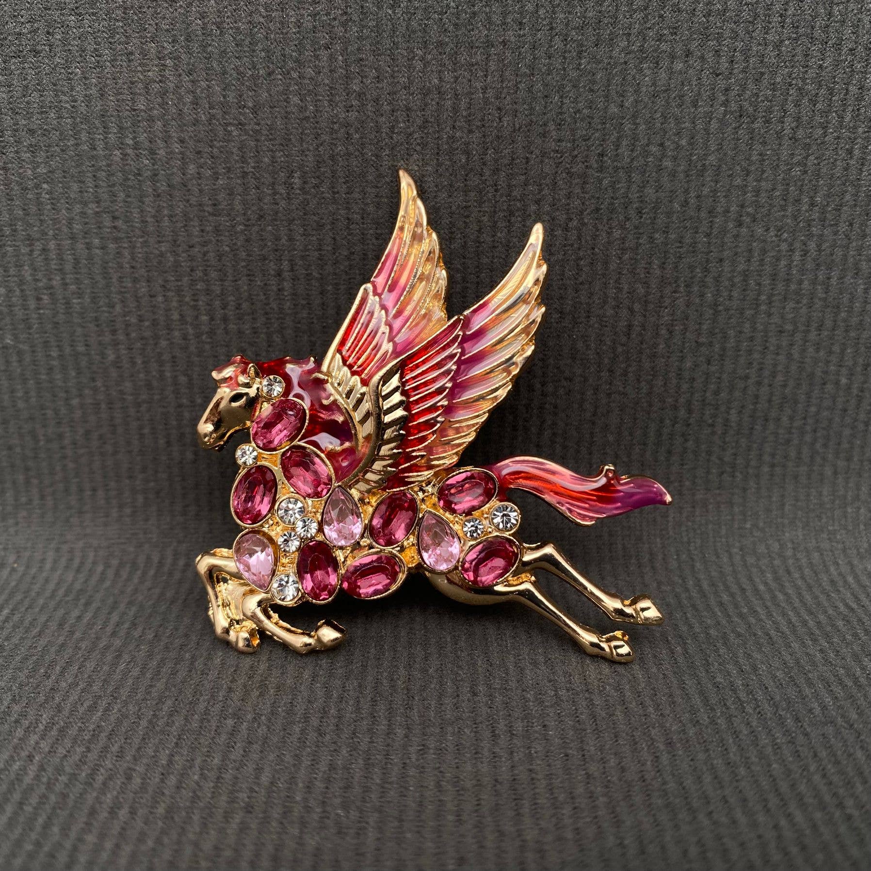 Gold pegasus brooch with ruby gemstones held in a hand against a gray background