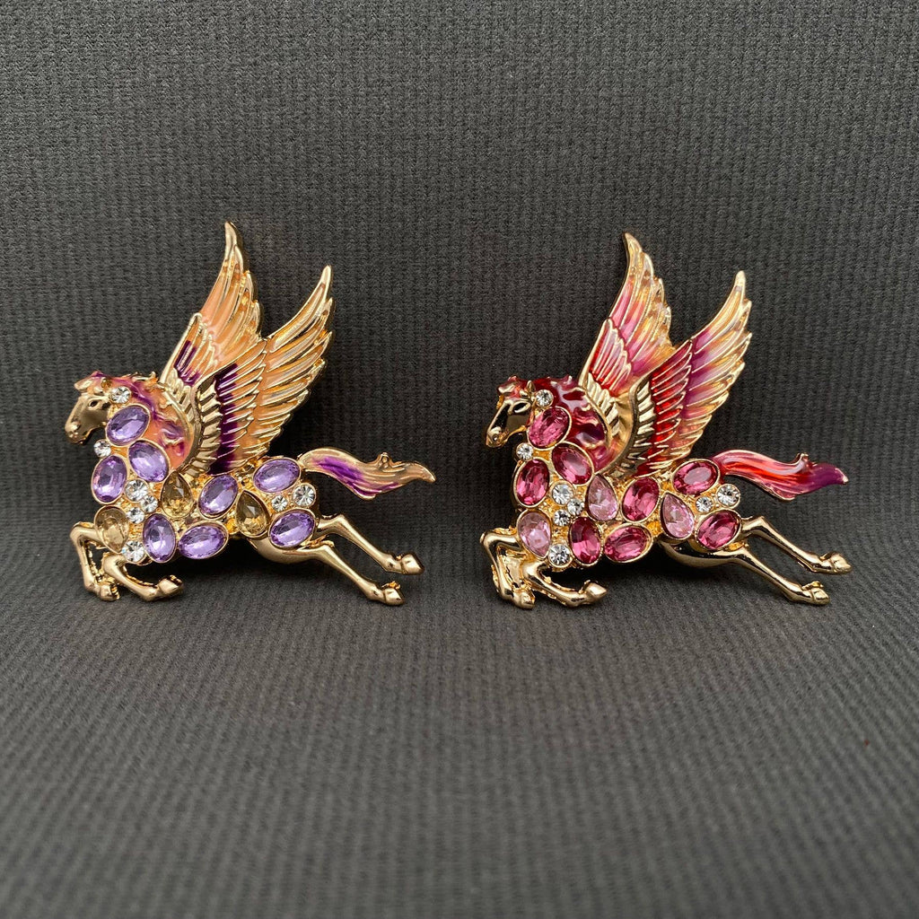 Two colorful pegasus brooches with ruby and purple gemstones, on a gray background