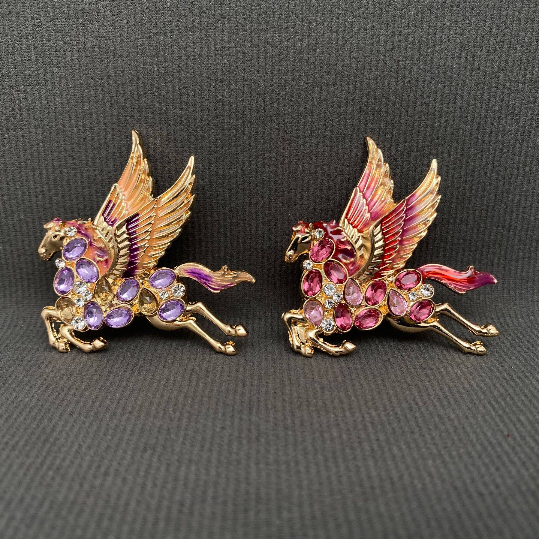 Two colorful pegasus brooches with ruby and purple gemstones, on a gray background