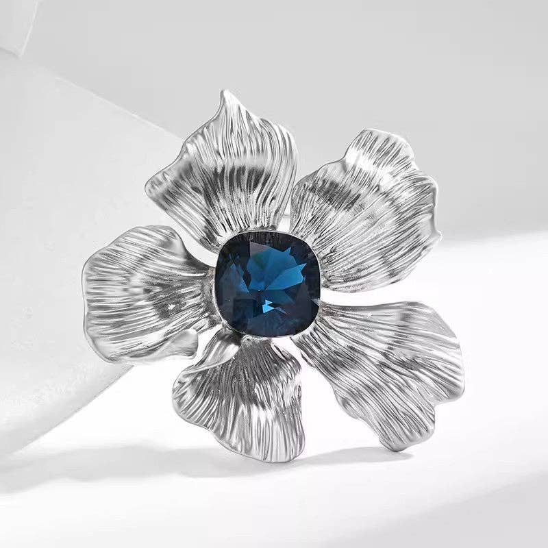 Silver flower-shaped brooch with a blue gemstone on a white background