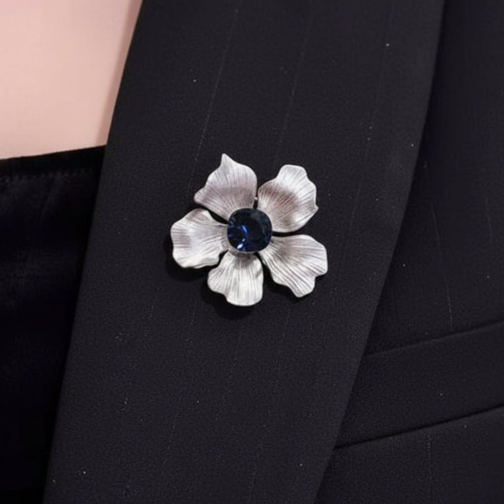 Silver flower-shaped brooch with a blue gemstone pinned on woman's black suite
