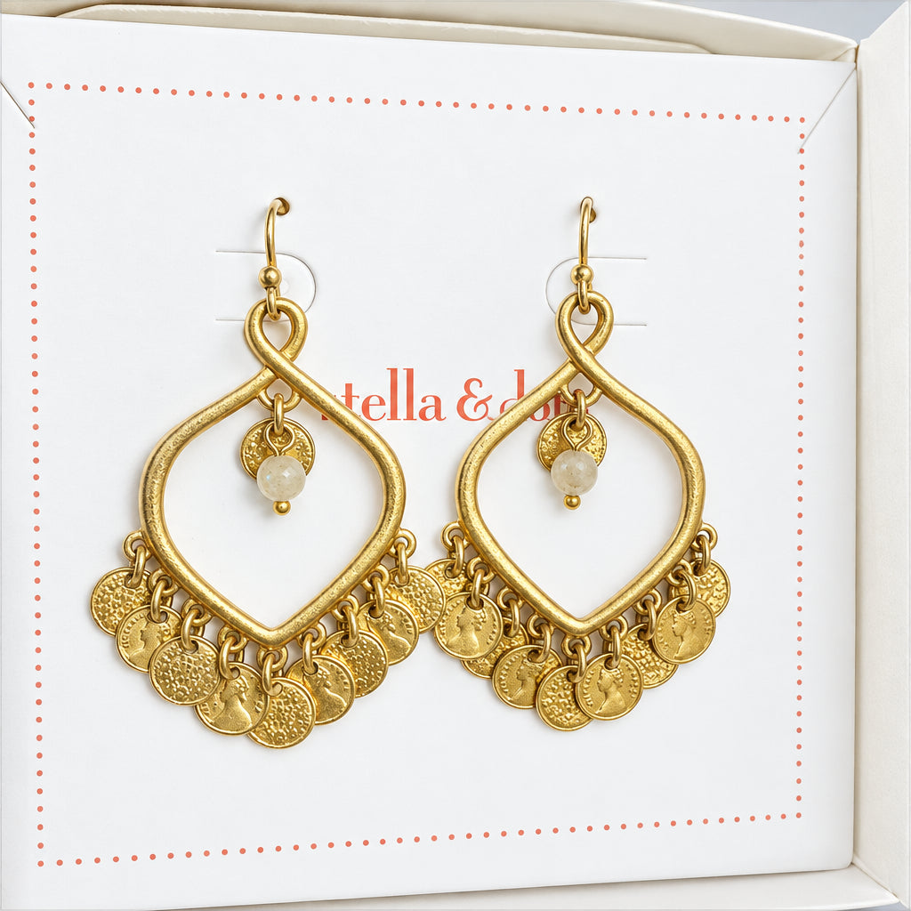 A pair of gold-toned dangle earrings displayed inside a white designer gift box. The earrings feature a large open teardrop shape with a small bead and dangling coin charms at the bottom.