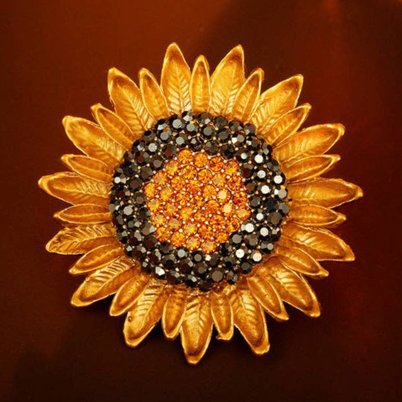 Sunflower-shaped brooch with gold petals and gemstone center on a orange background