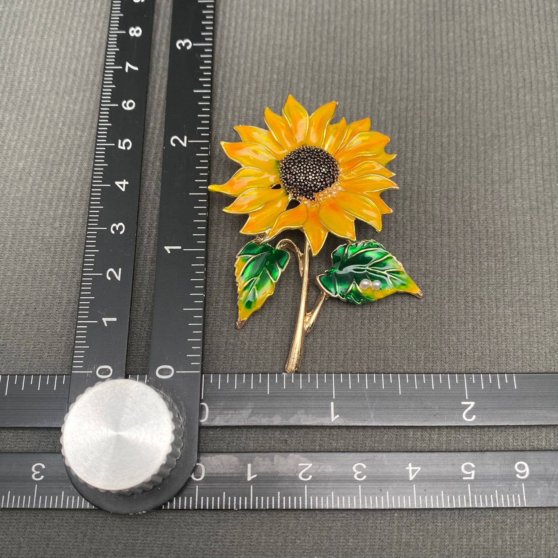 Sunflower-shaped brooch with green leaves on a gray background