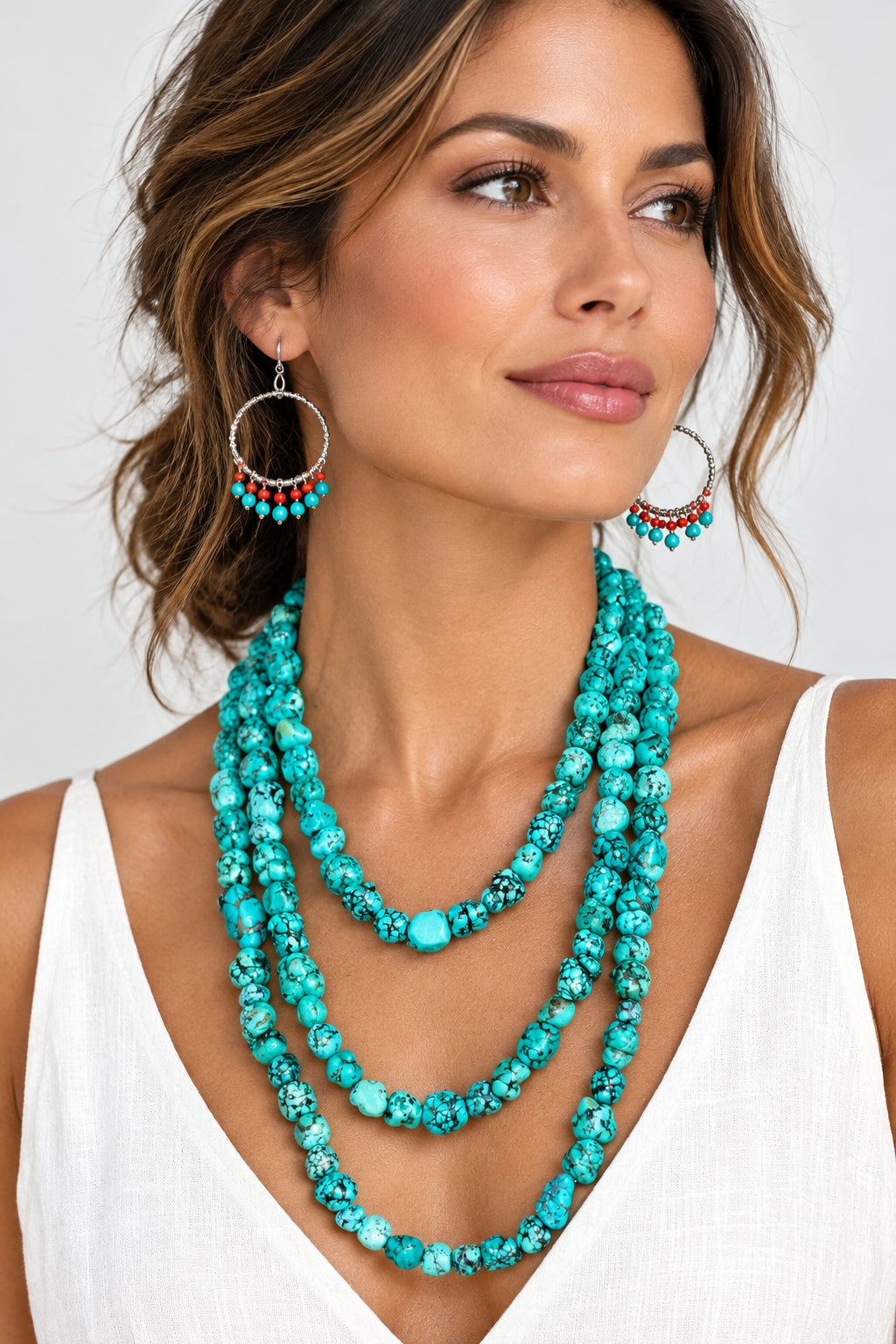 A woman wearing a long multi-strand turquoise and marbled bead necklace, with matching turquoise beaded earrings.