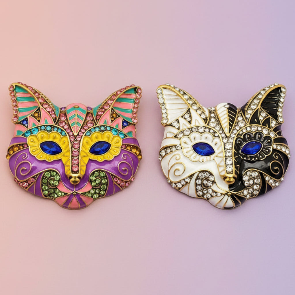 Two decorative cat mask brooches, one colorful and one black and gold, on a pastel background