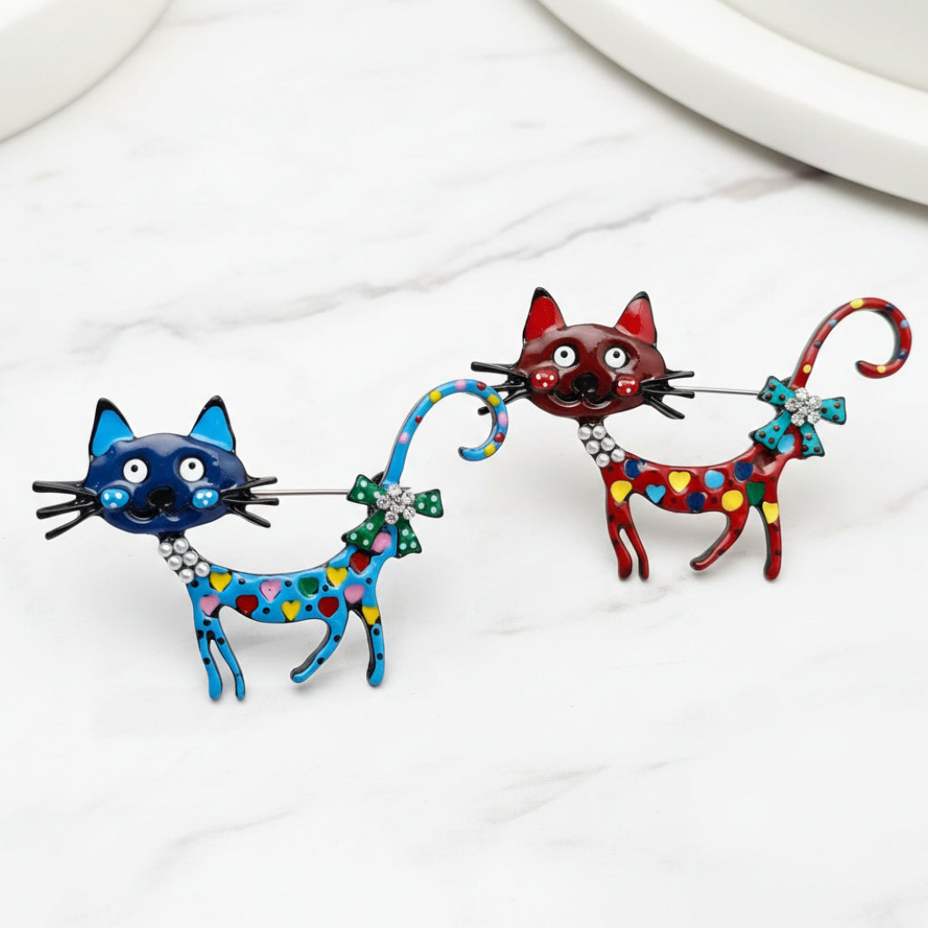 Two colorful cat-shaped brooches on a white marbled background