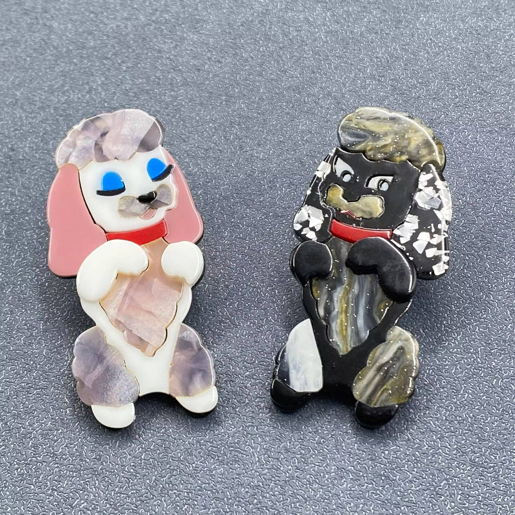 Two dog-shaped brooch with pink, black, white, and red colors on a gray background