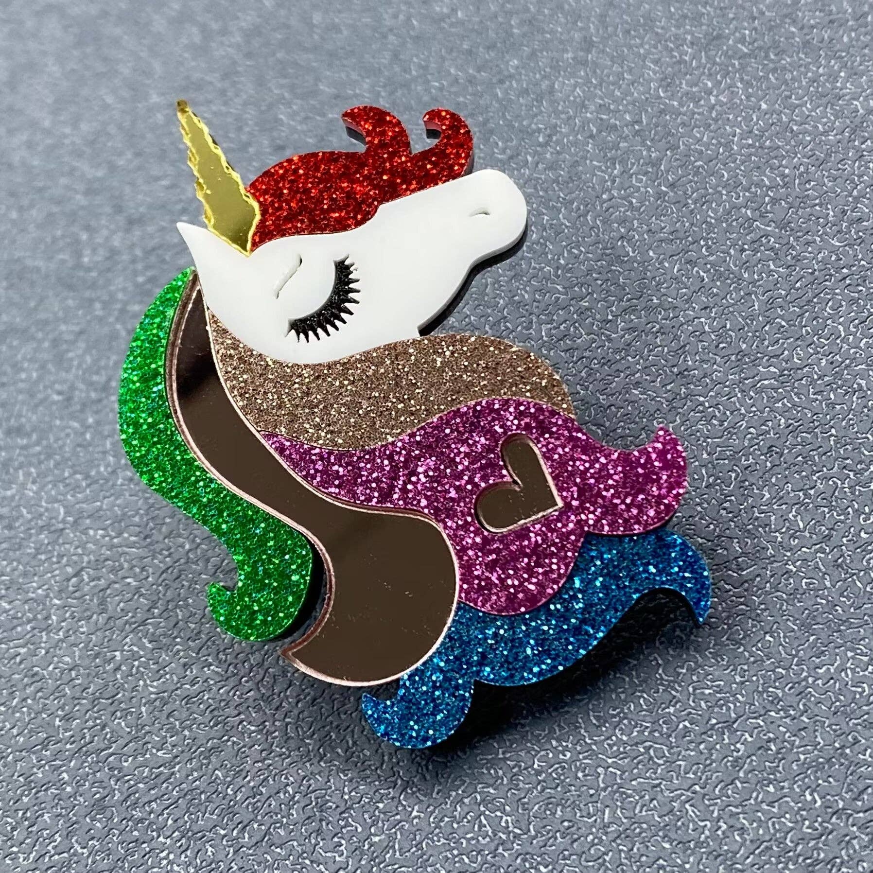 Glittery unicorn pin with multicolored mane and tail on a textured gray background